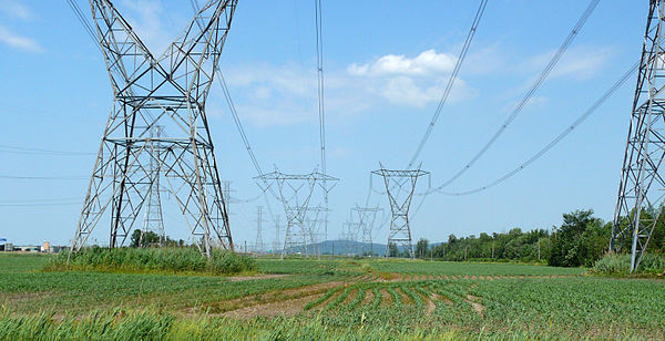 A photo of hourglass-shaped high-trasmission towers carrying electrical wires across a landscape.